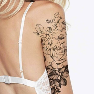 May include: A black and white line drawing tattoo design of roses and a bird on a person's arm.