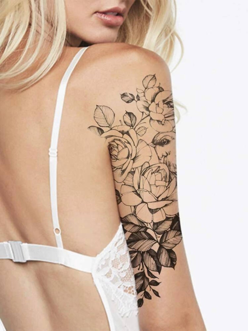 May include: A black and white line drawing tattoo design of roses and a bird on a person's arm.