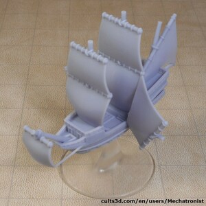 Puede incluir: Maqueta de velero gris claro con múltiples velas y un casco detallado. El barco está montado sobre un soporte transparente. Las velas están completamente extendidas y el barco parece ser de plástico. Modelo para exhibición o pasatiempo.