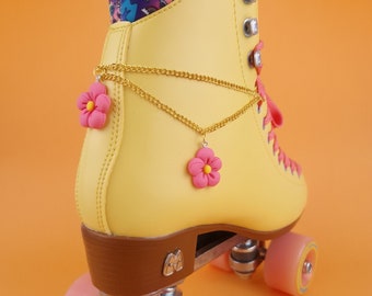 May include: Yellow roller skates with pink flower charms on a gold chain. The skates have brown wheels and a brown base.