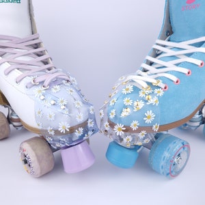 May include: Two pairs of roller skates with daisy-patterned toe guards. One pair is white with lavender laces and purple wheels, the other is blue with white laces and blue wheels.