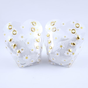 May include: Two clear plastic heart-shaped containers with white daisy patterns and gold accents. The containers are empty.