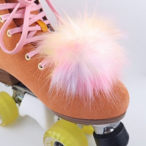 Pu&ograve; includere: Roller skate arancioni con ruote gialle e un pompon soffice rosa e bianco attaccato alla punta dello skate.