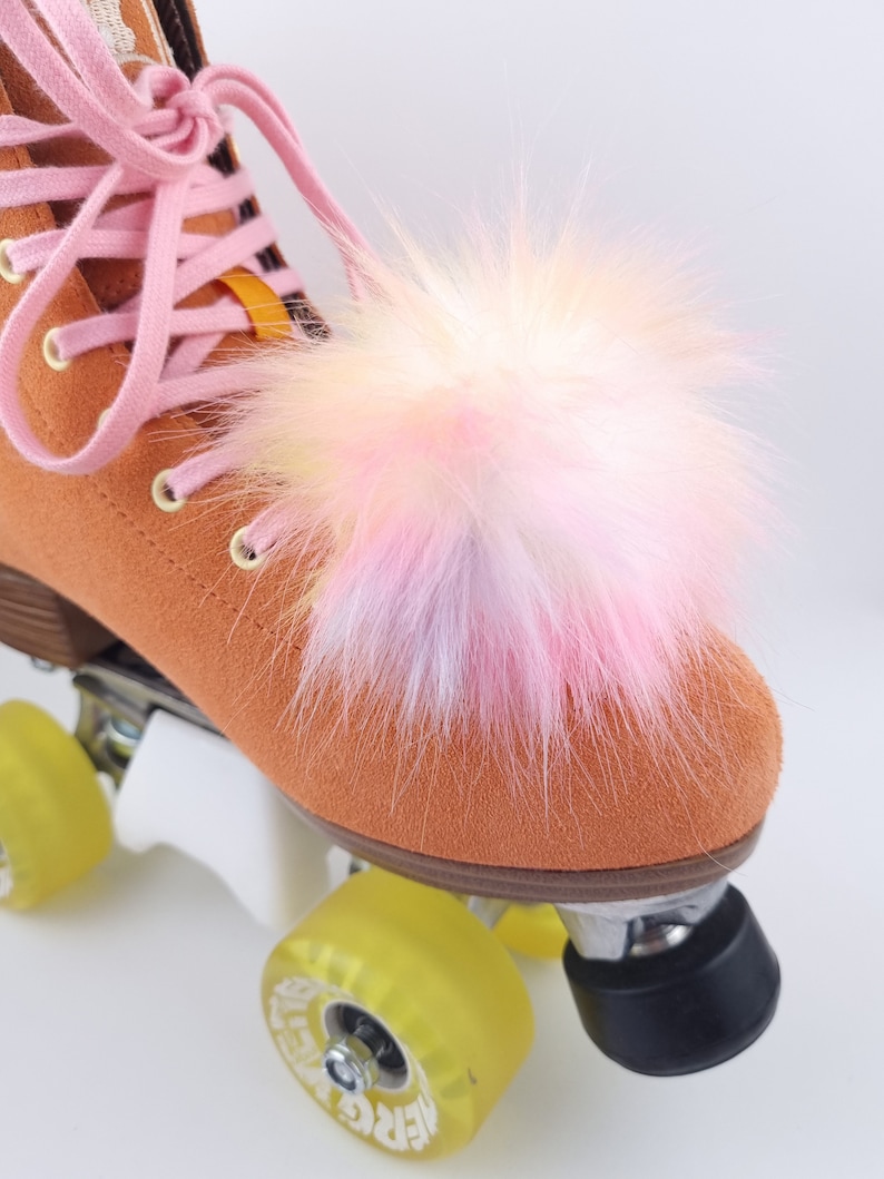 Pu&ograve; includere: Roller skate arancioni con ruote gialle e un pompon soffice rosa e bianco attaccato alla punta dello skate.