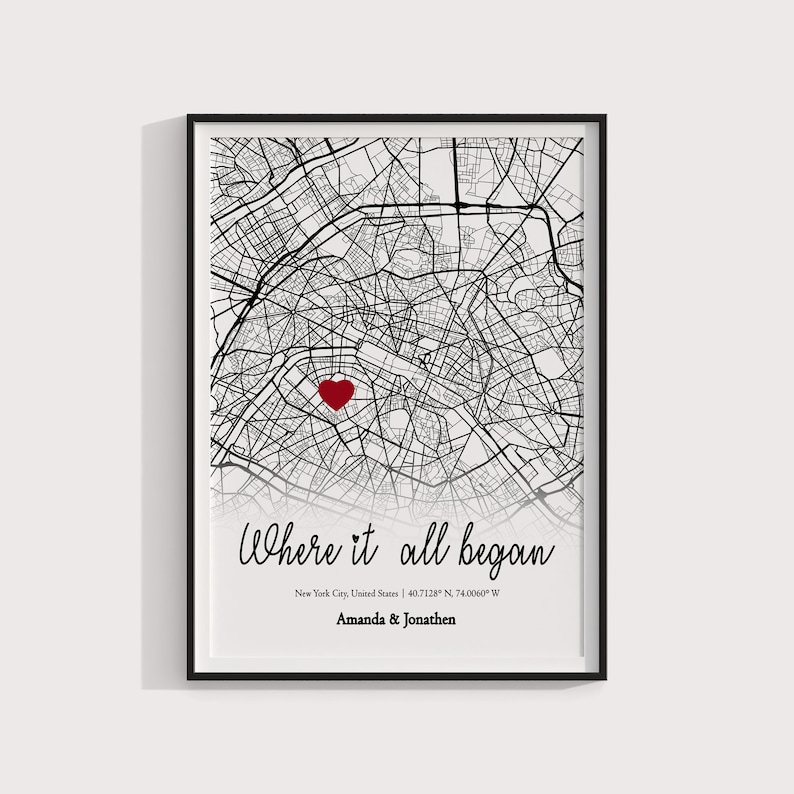 Op de afbeelding: Een zwart-witte kaart van New York City met een rood hart dat een locatie markeert. De tekst "Where it all began" is in cursief onder de kaart geschreven, samen met de co&ouml;rdinaten "40.7128&deg; N, 74.0060&deg; W" en de namen "Amanda & Jonathen".