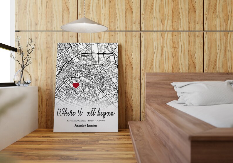 Op de afbeelding: Een zwart-witte kaartprint met een rood hart dat een locatie markeert. De tekst "Where it all began" staat onder de kaart, samen met de stad, de staat en de co&ouml;rdinaten. De namen "Amanda & Jonathan" staan onder de co&ouml;rdinaten.