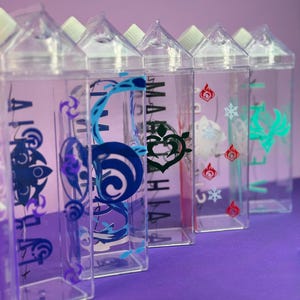 May include: A row of clear plastic water bottles with white caps. Each bottle has a different colorful graphic design on the front, including blue, green, and red symbols. The bottles are arranged on a purple surface.