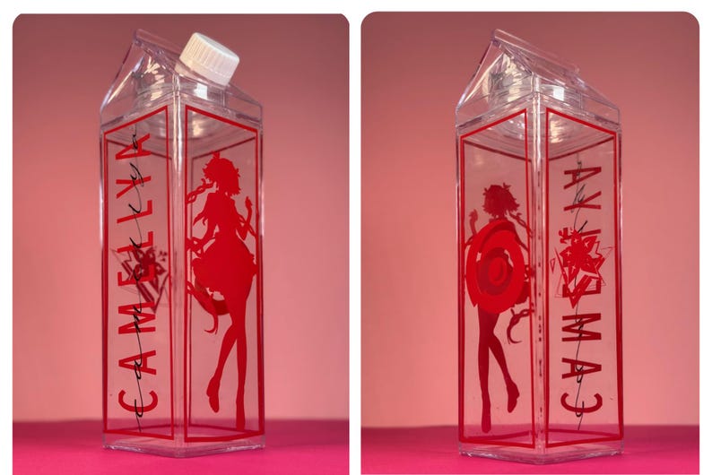 May include: Clear plastic milk carton-shaped bottle with a white cap. The bottle has red text and a red silhouette of a woman. The text reads "CAMELIA".