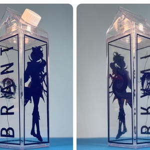 May include: Clear plastic water bottle with a white cap, shaped like a milk carton. The bottle features a dark blue silhouette of a character and the word "BRONT" in dark blue.