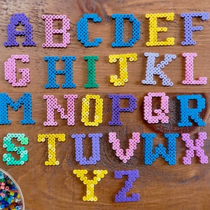 May include: A colourful alphabet made of plastic beads. Each letter is a different colour and is arranged in alphabetical order. The beads are on a wooden surface.