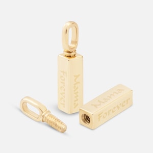 Op de afbeelding: Twee gouden metalen staafhangers met de woorden "Mama Forever" gegraveerd op elk. De hangers zijn gescheiden en een ligt op zijn zijde.