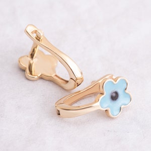 May include: A pair of gold earrings featuring a blue flower design. The flower has a white centre and a black dot in the middle.