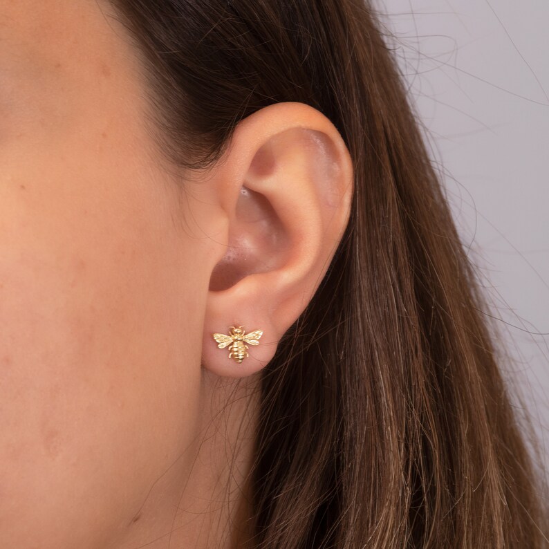 May include: A pair of gold bee stud earrings. The earrings are small and delicate, and they feature a realistic bee design.