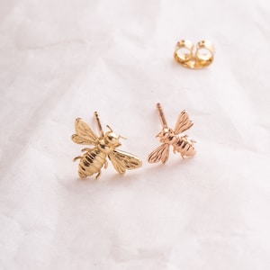 May include: A pair of gold bee stud earrings. The earrings are made of shiny gold metal and feature a detailed bee design.