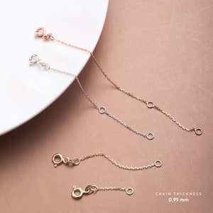 May include: Three gold chains of different lengths, each with a clasp and a jump ring. The chains are on a white plate against a light brown background. The text "CHAIN THICKNESS 0.95 mm" is at the bottom of the image.