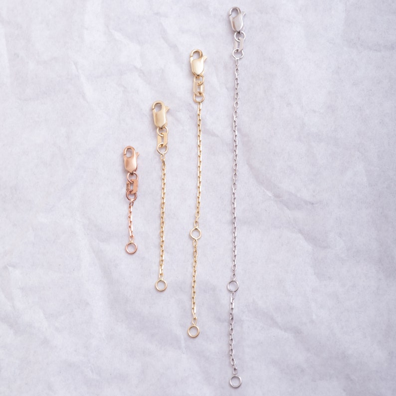 May include: Four gold and silver chain extenders of different lengths. The extenders are made of a delicate chain with a lobster clasp on one end and a jump ring on the other.