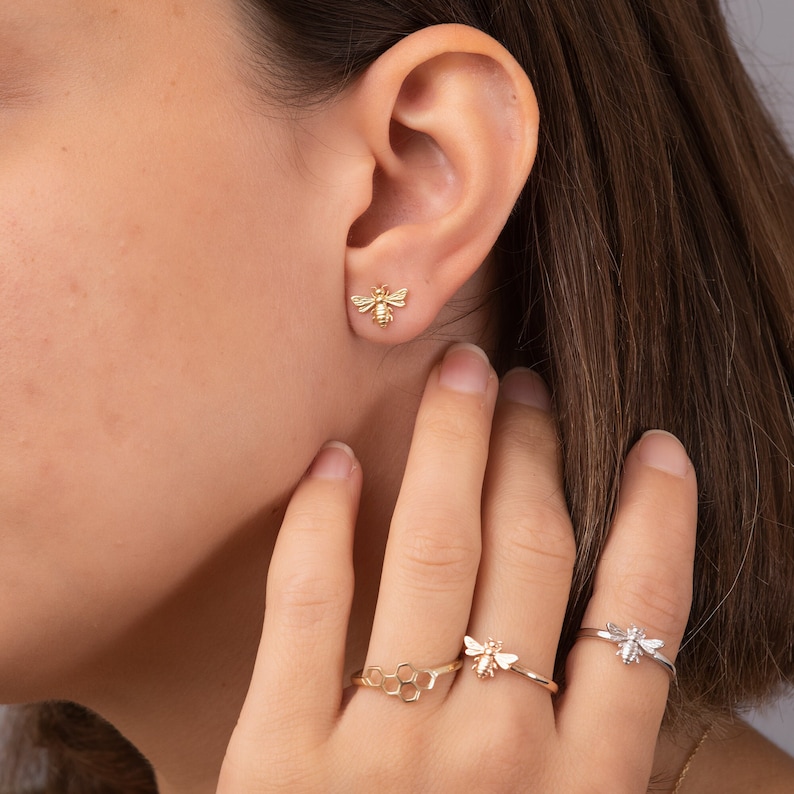 May include: Gold bee earrings and rings. The earrings are small and feature a detailed bee design. The rings feature a bee design and a honeycomb design.