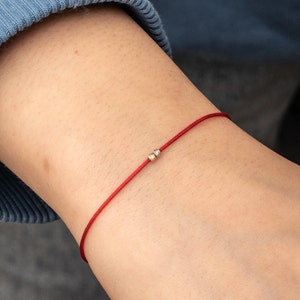 Pode incluir: Um bracelete de corda vermelha com duas pequenas contas douradas.