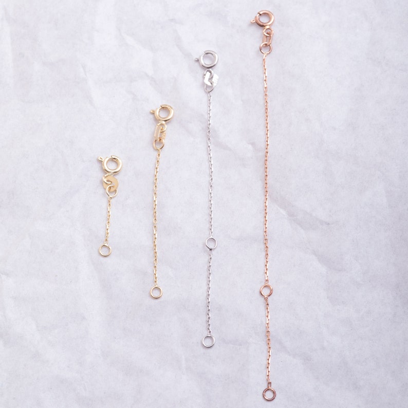 May include: Three gold chain extenders of different lengths. The extenders are made of a delicate chain with a lobster clasp on one end and a jump ring on the other.