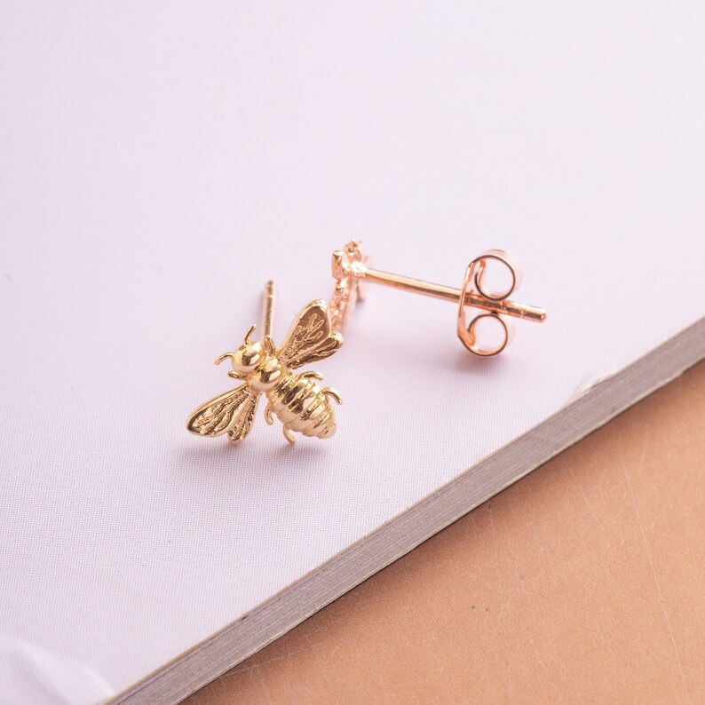 May include: A pair of gold bee stud earrings with a post and butterfly back.