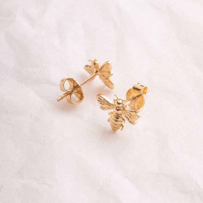 May include: A pair of gold bee stud earrings. The earrings are made of shiny gold metal and feature a detailed bee design.