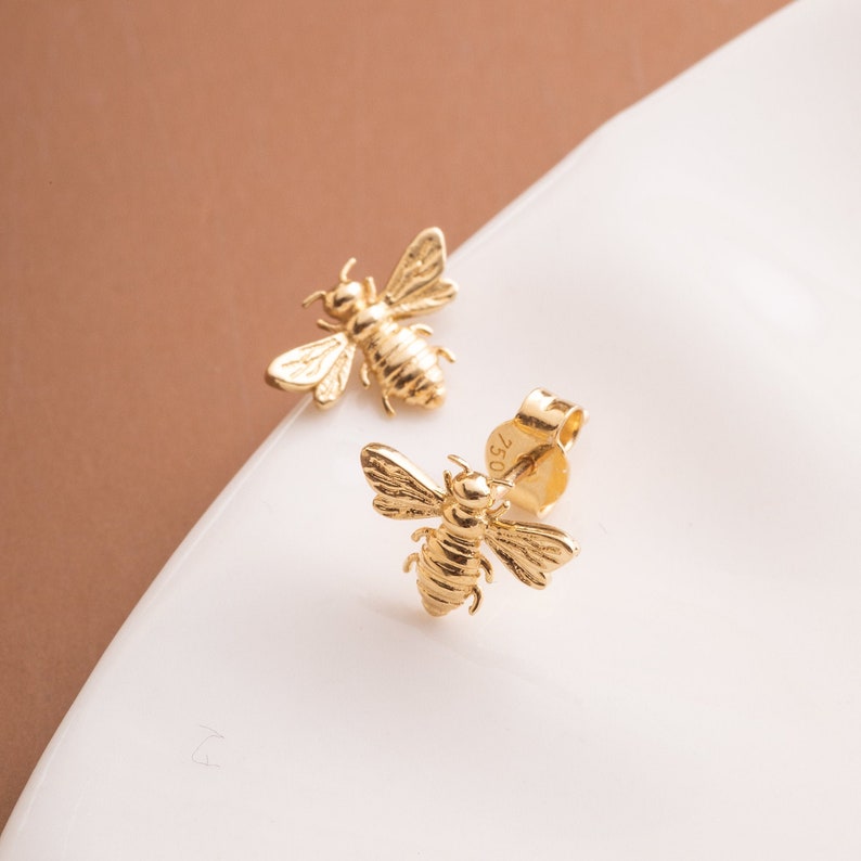 A pair of gold bee stud earrings. The bees are detailed and have a textured finish.