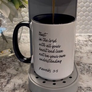 May include: White ceramic mug with a black handle and black rim. The mug has a black inscription that reads "trust in the lord with all your heart and lean not on your own understanding proverbs 3:5".