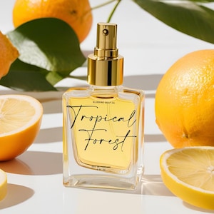 May include: A clear glass bottle of perfume with a gold cap and sprayer. The bottle is labeled "Tropical Forest" and "Blueberry Soap Co.". The bottle is sitting on a white surface with lemons and oranges.