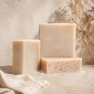 May include: Three rectangular bars of light beige soap arranged in a stack. The largest upright bar features the embossed text bluebyrd in the center. The soap has a smooth surface with a slightly textured, uneven bottom edge on the base bar.