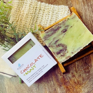May include: A bar of green and brown swirl soap with the text "BLUEBYRD SOAP CO CHOCOLATE + MINT ARTISAN HANDMADE ALL NATURAL SOAP MADE WITH BITS OF REAL ORGANIC CHOCOLATE VEGAN COLD-PROCESSED 1.5 OZ BLUEBYRDSOAPS.COM" on the white label.