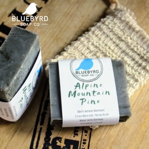 May include: Two bars of dark gray soap with white labels. The labels have the text "BLUEBYRD SOAP CO." and "Alpine Mountain Pine". The soap is handmade, cold-processed, vegan, and made with natural cleansing clays.