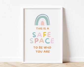 May include: A framed print with a white border. The print features a rainbow and the words "THIS IS A SAFE SPACE TO BE WHO YOU ARE" in colorful, playful lettering. The background is white.