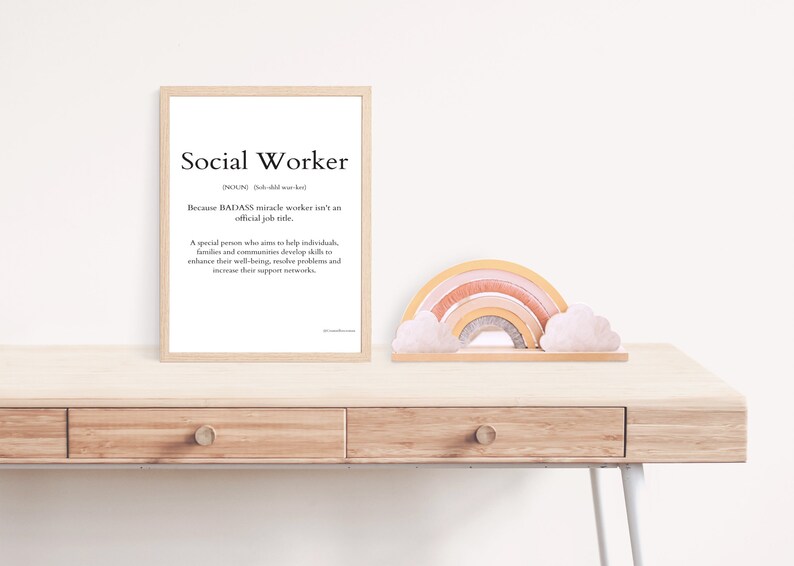 May include: A framed print with a white background and black text that reads "Social Worker" and a definition of the word. The print is on a wooden desk with a rainbow-coloured wooden toy and two white clouds.