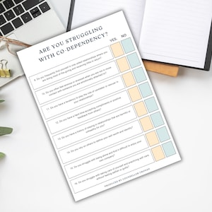 K&ouml;nnte beinhalten: Ein gedrucktes Arbeitsblatt mit dem Titel &bdquo;ARE YOU STRUGGLING WITH CO-DEPENDENCY?&ldquo; mit einer Checkliste von Fragen. Das Arbeitsblatt liegt auf einer wei&szlig;en Oberfl&auml;che mit einem Laptop, einer Brille, einem Notizbuch und einem Stift. Der Text ist schwarz und die K&auml;stchen sind gelb und blau.