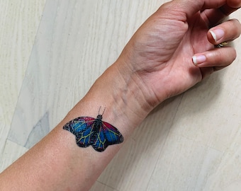 May include: A temporary tattoo of a colorful butterfly with blue, red, and yellow accents on a person's wrist.