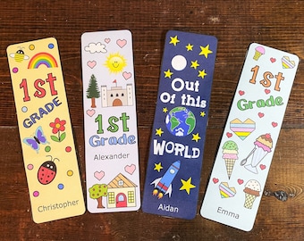 May include: Four colourful bookmarks with different designs and names. The bookmarks are decorated with illustrations of a rainbow, a castle, a rocket, and ice cream cones. The text on the bookmarks reads "1st Grade" and includes the names Christopher, Alexander, Aidan, and Emma.