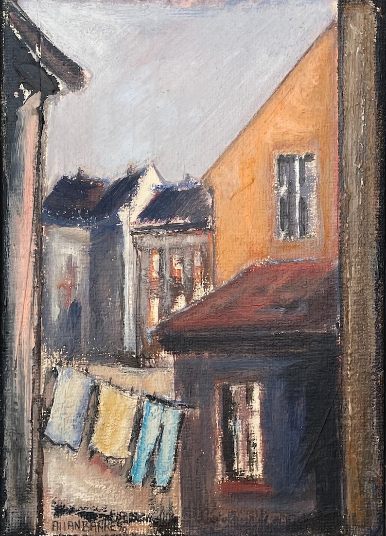 May include: A painting of a narrow street scene with buildings on either side. The buildings are painted in shades of brown, orange, and gray. There are clothes hanging on a line in the foreground. The painting is signed "Julian Banks" in the lower left corner.