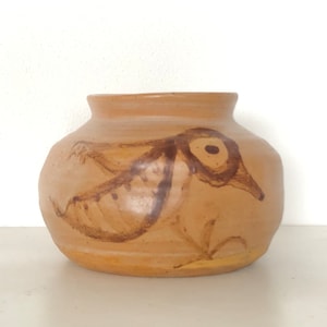 以下が含まれることがあります： 茶色の手描きの鳥のデザインが施された、ベージュ色の陶器の花瓶。 花瓶は丸みを帯びたボディとわずかにフレアしたリムを持っています。 鳥はシンプルな線と形で描かれており、フォークアートのような雰囲気です。