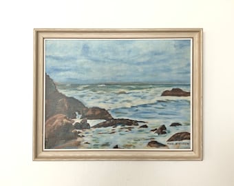 May include: A framed painting of a seascape with rocky cliffs and crashing waves. The sky is a light blue with white clouds. The painting is signed "Paul Nielsen".