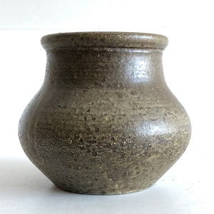 Puede incluir: Un jarrón de cerámica marrón con un esmalte moteado. El jarrón tiene un cuerpo redondeado y una abertura ancha.