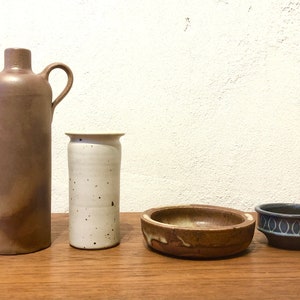 Peut inclure: Ensemble de quatre pièces en céramique, comprenant une bouteille brune avec une anse, un vase blanc moucheté, un bol brun avec un glaçage blanc et un bol bleu et blanc avec un motif géométrique.