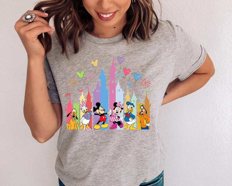 May include: A heather gray short-sleeve t-shirt featuring a colorful graphic print of Disney characters including Mickey Mouse, Minnie Mouse, Donald Duck, Daisy Duck, Goofy, and Pluto standing in front of a stylized castle with floating balloons.