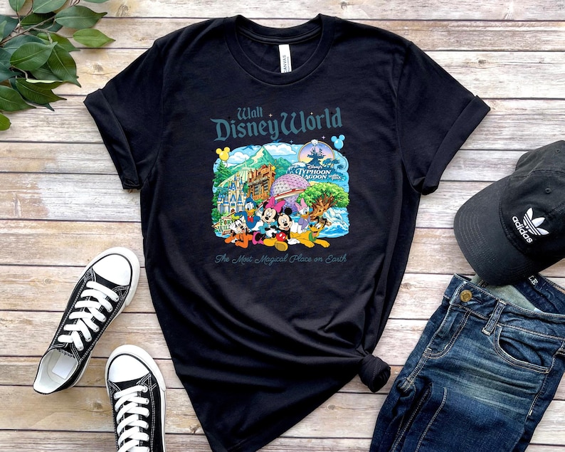 Op de afbeelding: Een zwart t-shirt met korte mouwen en een kleurrijke afbeelding van Walt Disney World-bezienswaardigheden en personages, waaronder Mickey Mouse, met de tekst "Walt Disney World" en "The Most Magical Place on Earth" op de borst.