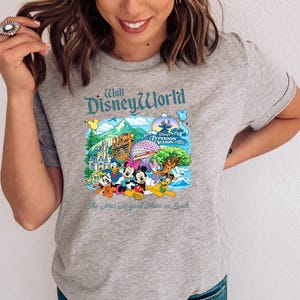 Op de afbeelding: Een grijs gem&ecirc;leerd t-shirt met een kleurrijke grafische print van Walt Disney World bezienswaardigheden en personages. Het ontwerp bevat Mickey Mouse, Minnie Mouse, Donald Duck, Goofy en Pluto, met de tekst Walt Disney World en The Most Magical Place on Earth.