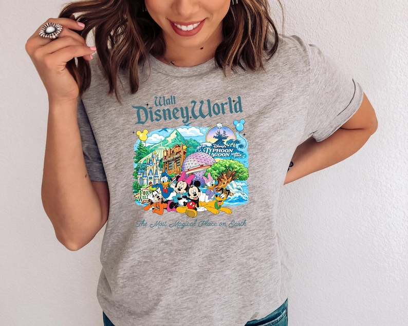 Op de afbeelding: Een grijs gem&ecirc;leerd t-shirt met een kleurrijke grafische print van Walt Disney World bezienswaardigheden en personages. Het ontwerp bevat Mickey Mouse, Minnie Mouse, Donald Duck, Goofy en Pluto, met de tekst Walt Disney World en The Most Magical Place on Earth.