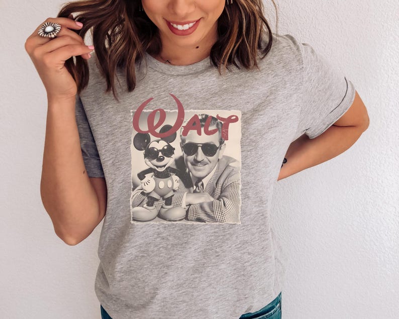 Puede incluir: Una camiseta gris jaspeado de manga corta con un estampado gr&aacute;fico de una fotograf&iacute;a en blanco y negro que muestra a un hombre y un rat&oacute;n de dibujos animados con gafas de sol. La palabra Walt est&aacute; impresa en una fuente roja grande.