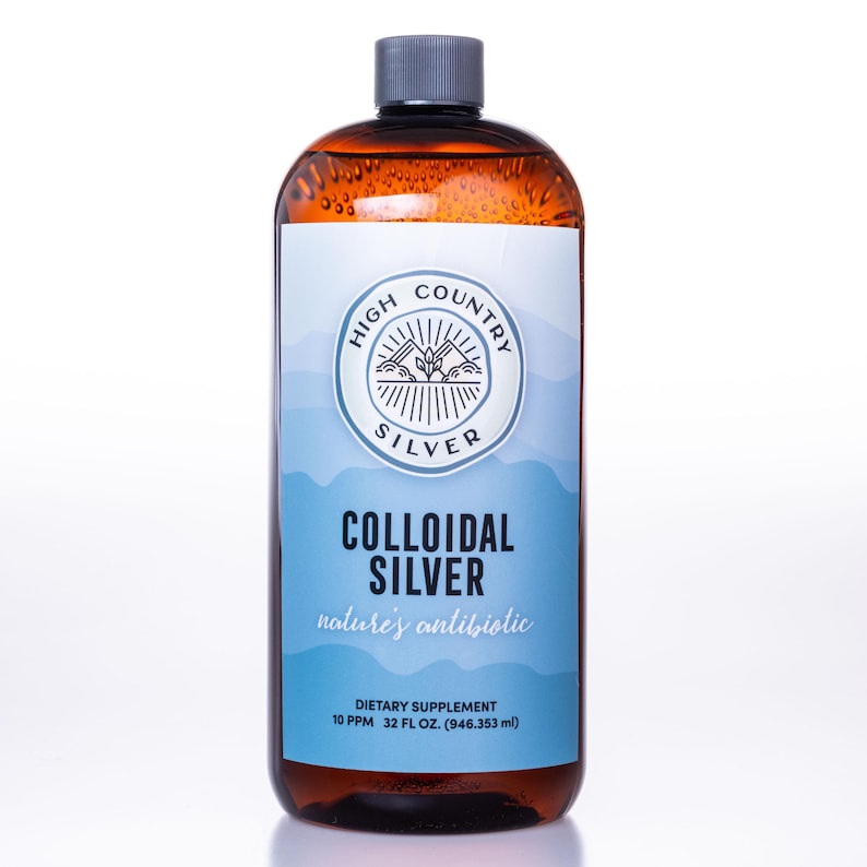 Op de afbeelding: Een bruine glazen fles met een grijze dop, met het label "High Country Silver Colloidal Silver". Het etiket heeft een blauw-wit ontwerp met de tekst "nature's antibiotic". De fles bevat 946,353 ml van een voedingssupplement.