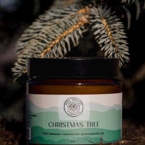 May include: A brown glass jar candle with a white label that says "High Country Candles" and "Christmas Tree". The label also says "100% beeswax + coconut oil + pure essential oils". The candle is sitting on a bed of pine needles.