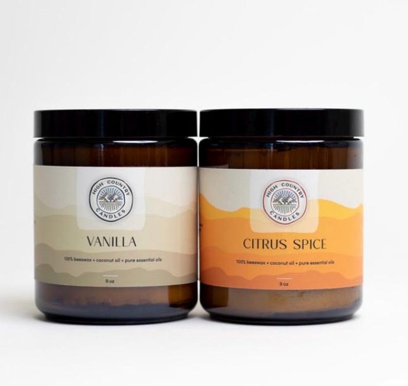 May include: Two amber glass candle jars with black lids. The labels are white with brown text and a logo that says "High Country Candles". The left jar is labelled "Vanilla" and the right jar is labelled "Citrus Spice". Both jars are 9 oz.