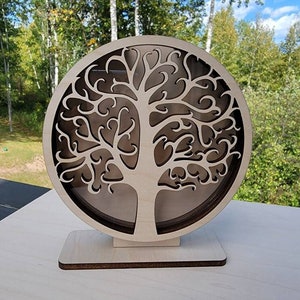 May include: A wooden tree of life sculpture with intricate details, standing on a small wooden base. The tree is carved in a circular shape and has a delicate, swirling design.